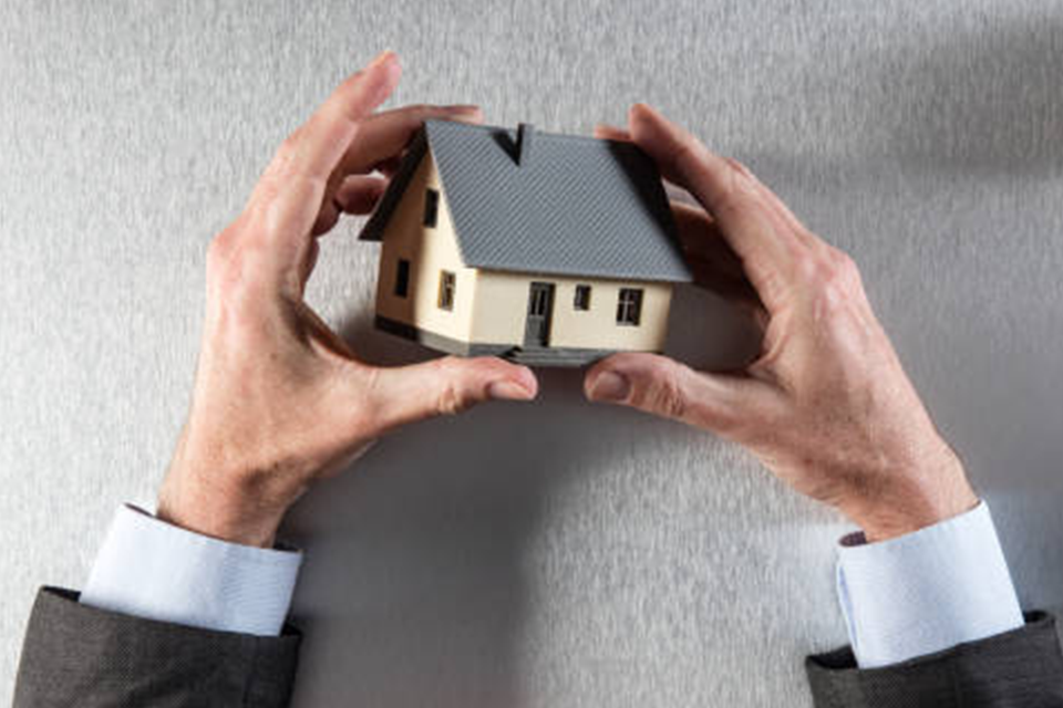 Image of a papir of hands holding a miniature model of a home.