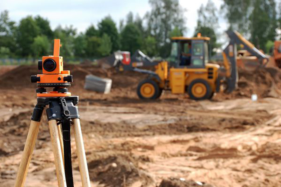 Image of a construction site with a survey camera overlooking a backhoe. 