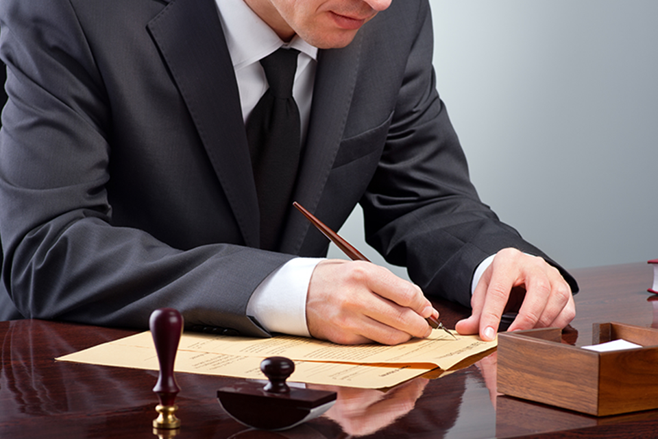 Image of a man in a suit and tie signing legal documents.