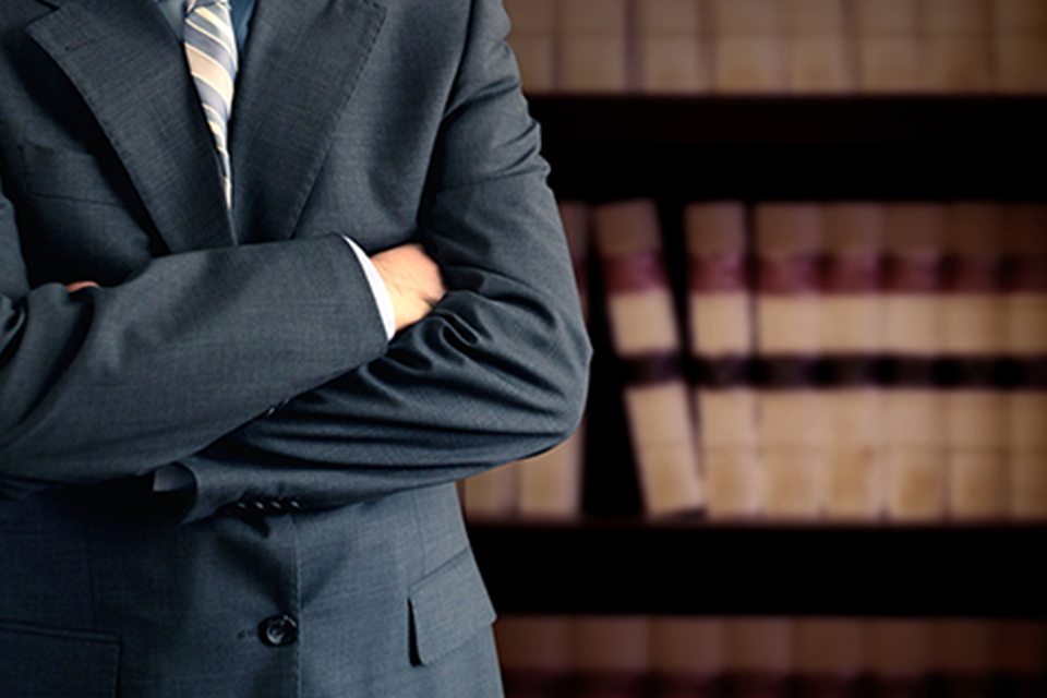 Image of a man with his arms folded in front, standing in front of a bookcase.